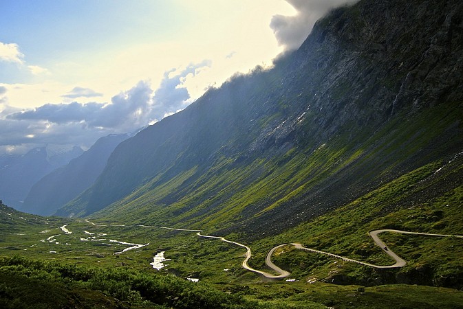 Klikatá horská silnice Trollstigen v Norsku obklopená zelenými svahy a vysokými vrcholy hor pod zataženou oblohou