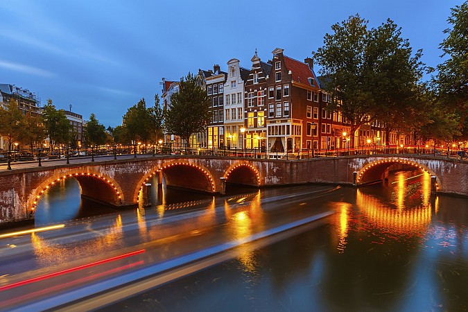 Amsterdam, osvětlený most přes kanál s historickými domy při večerním soumraku