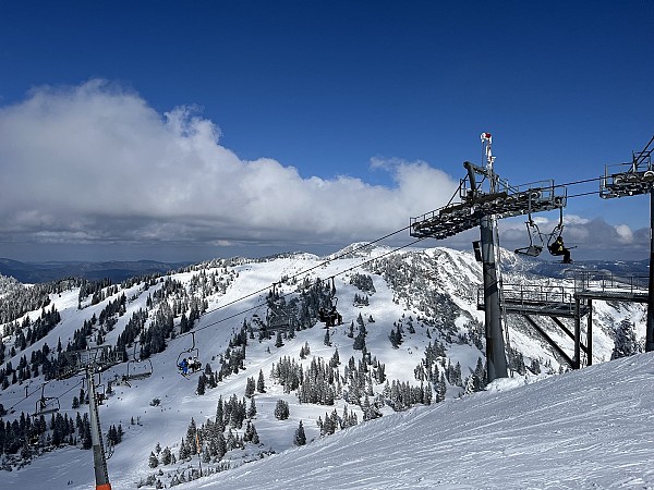 Lanovka stoupá nad zasněženými horami s výhledem na zasněžené vrcholky a modrou oblohu