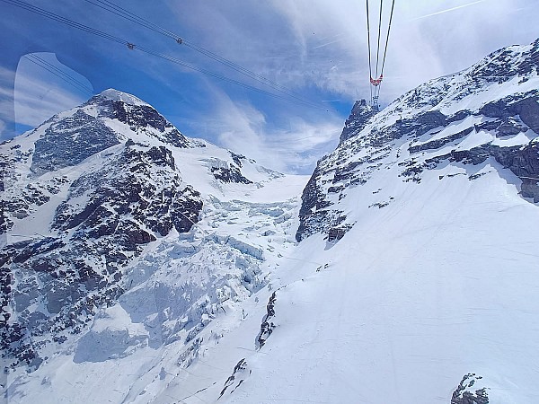 Lanovka stoupající nad zasněženými horskými svahy a ledovcem pod modrou oblohou