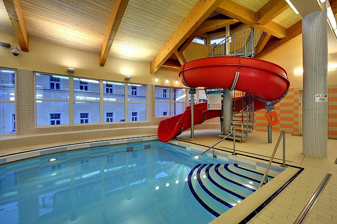 Krytý bazén s modrou vodou a červeným tobogánem