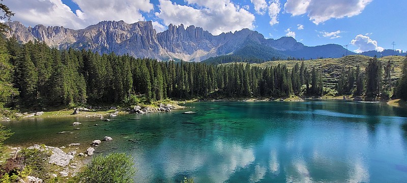 Průzračné horské jezero obklopené lesem, v hladině se odrážejí štíty majestátních Dolomit