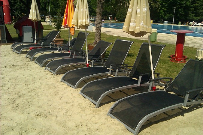 Řada černých lehátek na písečném povrchu s barevnými slunečníky u bazénu v lázních