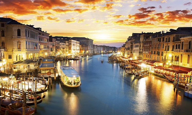 Canal Grande v Benátkách při západu slunce, osvětlené domy a lodě na vodě