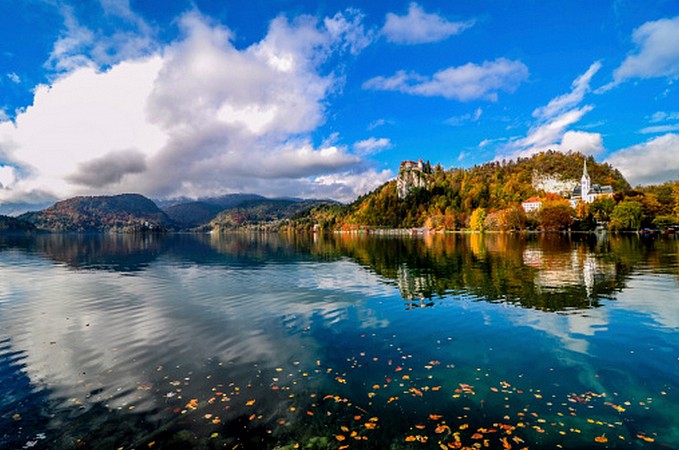Jezero Bled se středověkým hradem Bled na skalním útesu, odrážející se v klidné vodní hladině