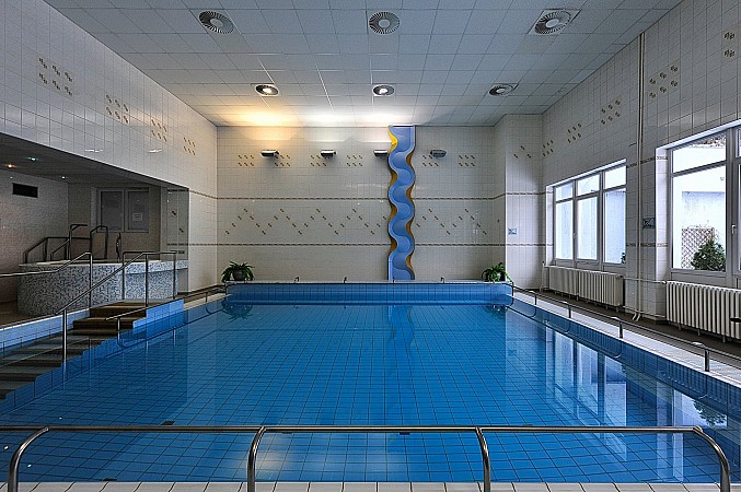 Vnitřní bazén s čistou modrou vodou, potápěčským prknem a velkými okny propouštějícími denní světlo