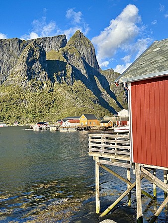 Červený dřevěný domek stojí u vodní hladiny obklopené strmými horskými svahy