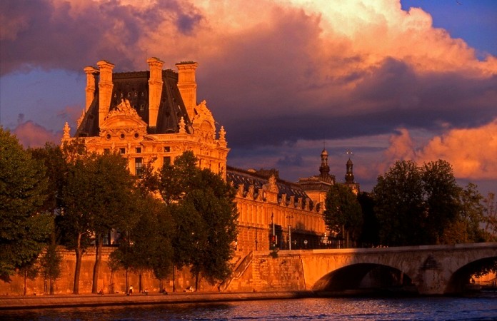 Historická budova muzea Louvre v Paříži je osvětlena teplým světlem zapadajícího slunce
