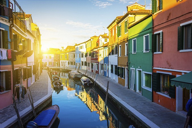 Úzký kanál s loďkami, lemovaný barevnými domy při západu slunce