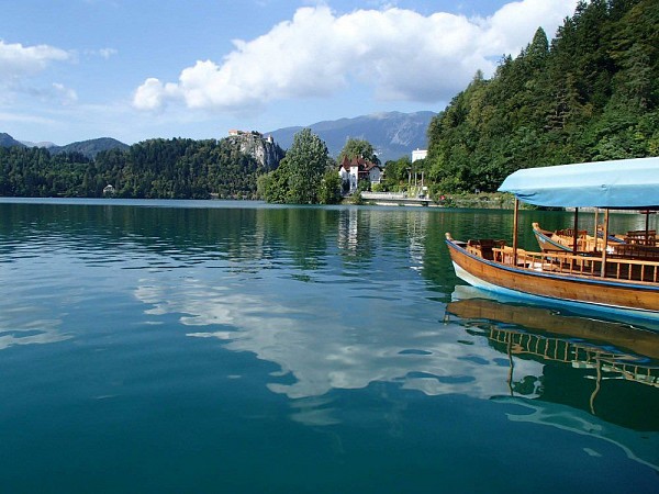 Dřevěná loďka na jezeře Bled ve Slovinsku, ostrov s kostelem a okolní hory