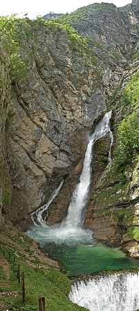 Vodopád Savica padající z vysoké skalní stěny do smaragdově zeleného jezírka, obklopený horami a lesy
