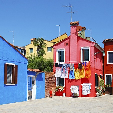 Barevné domy – modrý, červený, žlutý – se sušícím se prádlem na šňůrách před nimi