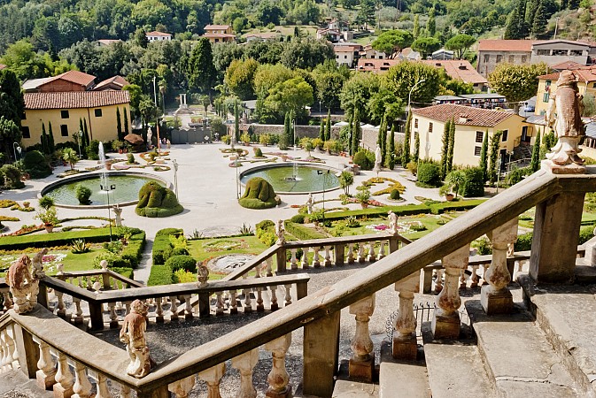 Široké kamenné schodiště vede dolů do udržované zahrady s fontánou, sochami a upravenými cestičkami
