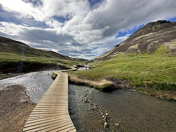 Dřevěný chodník vedoucí přes potok v travnatém údolí