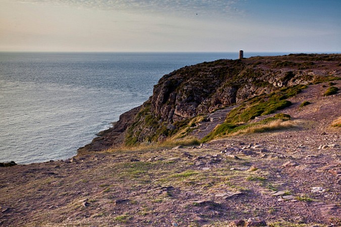 Strmý útes spadající do moře s majákem na jeho okraji