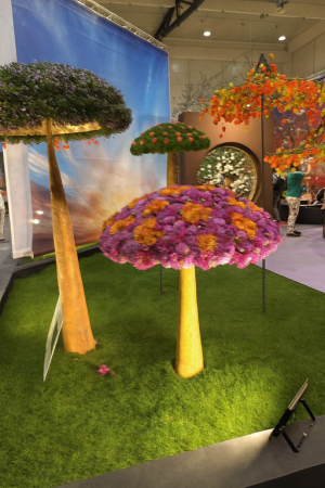 Květinové instalace ve tvaru stromů s barevnými korunami vytvořenými z květin, umístěné v interiéru na ploše s umělou trávou