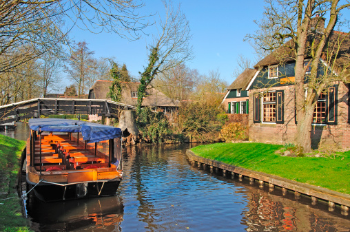 Úzký vodní kanál s dřevěným člunem a malebnými cihlovými domy se zahradami po obou stranách