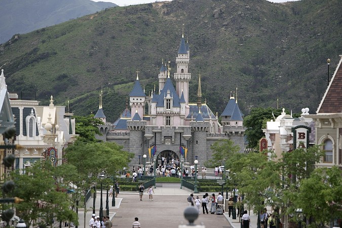 Zámek v Disneylandu s horským masivem a promenáda plná návštěvníků