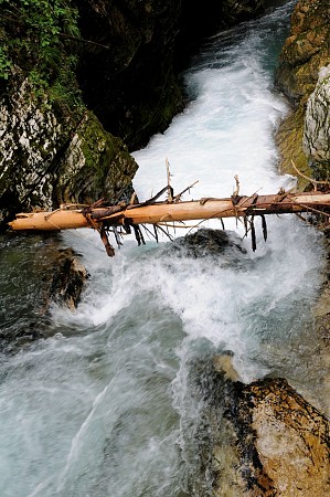 Dřevěná turistická lávka klenoucí se nad divokou, zpěněnou řekou v úzké skalní soutěsce