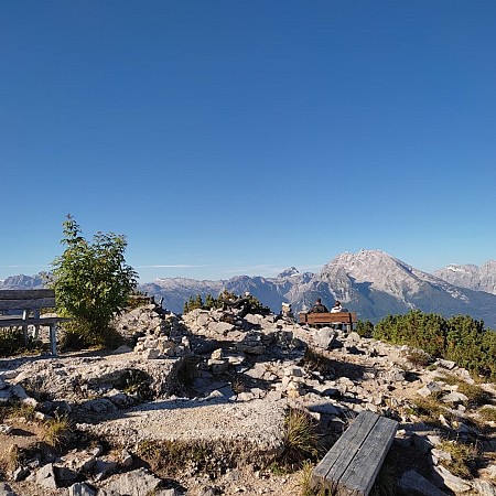 Kamenný vrchol s dřevěnými lavičkami a rozhledem na okolní horské masivy