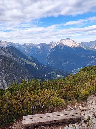 Dřevěná lavička na horské stezce s výhledem na zelené svahy a zasněžené vrcholky hor