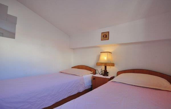 Pokoj se dvěma samostatnými postelemi s dřevěnými rámy a nočním stolkem s lampou mezi nimi