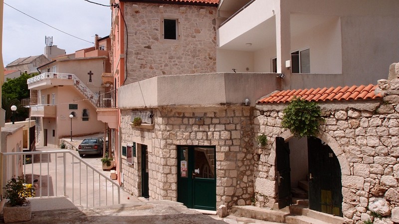 Úzká ulička lemovaná kamennými domy s dřevěnými okenicemi a obloukovým průchodem