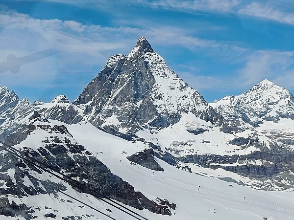 Strmý zasněžený štít hory se tyčí nad ledovcem pod jasně modrou oblohou