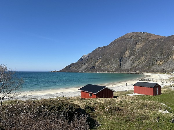 Pobřeží s nízkými budovami, skalnatým kopcem a otevřeným mořem pod jasnou oblohou