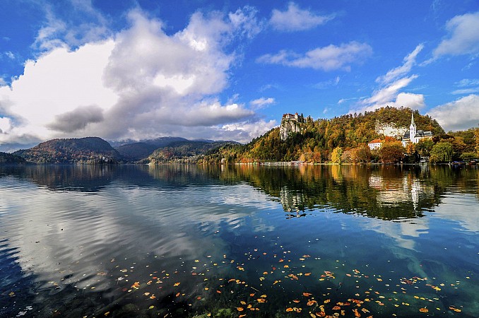 Jezero Bled ve Slovinsku s ostrovem, na kterém stojí kostel Nanebevzetí Panny Marie, obklopené horami a jasně modrou oblohou s mraky