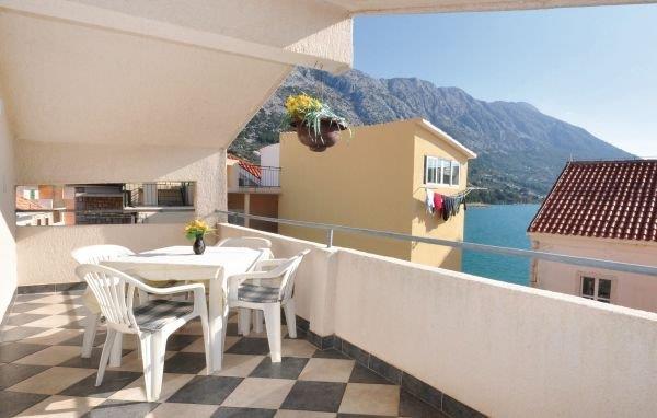 Balkon s bílým plastovým stolem a židlemi, květinami v truhlíku a výhledem na moře a hory