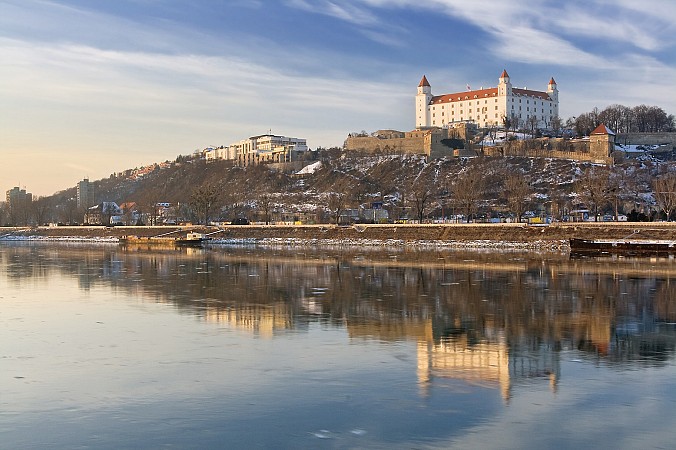 Bratislavský hrad osvětlený večerním sluncem, odrazující se na klidné hladině Dunaje