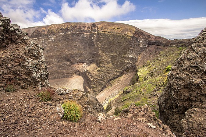 Horský kráter s holými skalami a řídkou vegetací leží pod částečně oblačnou oblohou