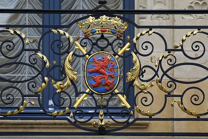 Kovaná brána se zlatými ozdobami a barevným erbem se lvem uprostřed