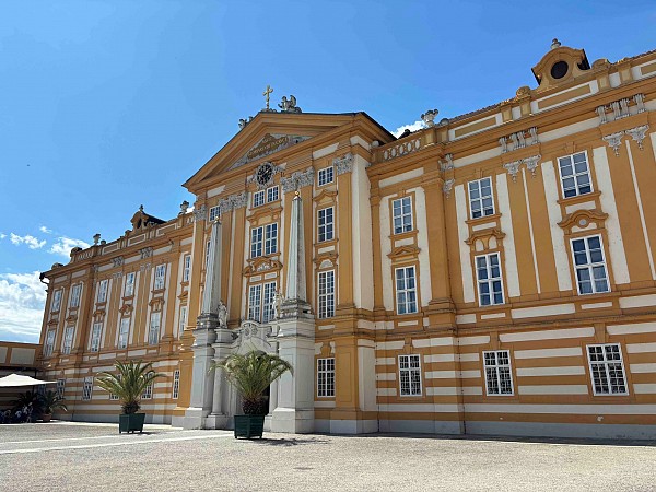 Klášter Melk, historická budova s okrovou fasádou a bílými detaily pod jasně modrou oblohou