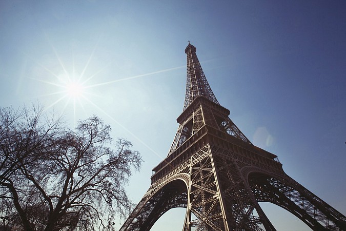 Paříž, Eiffelova věž proti jasné obloze se sluncem a větvemi stromů