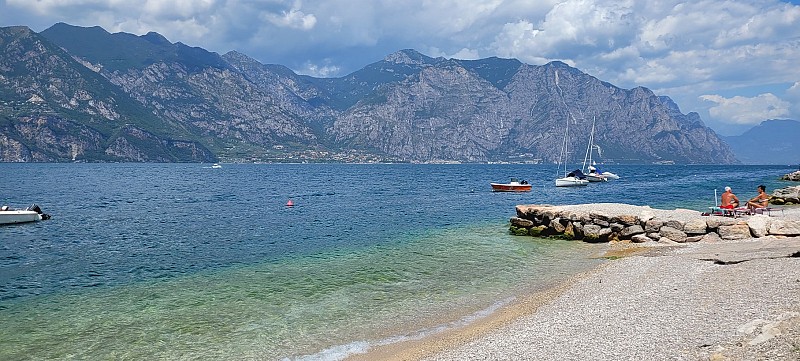 Pláž s jemným pískem u jezera, kde kotví malý člun u dřevěného mola