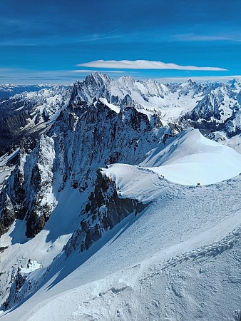 Rozsáhlá zasněžená horská krajina s ostrými štíty a ledovcovými svahy pod jasným modrým nebem