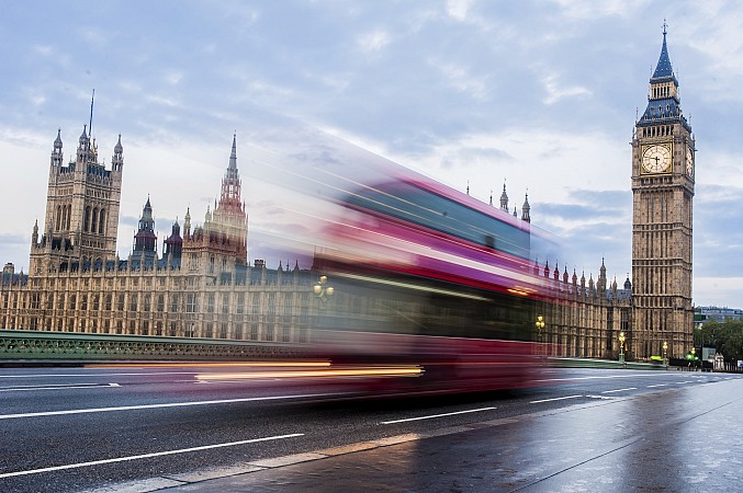 Červený dvoupatrový autobus v pohybu projíždí kolem Westminsterského paláce a věže Big Ben
