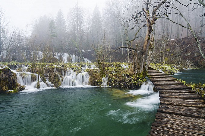 Dřevěná stezka vede podél tyrkysového jezera s kaskádovitými vodopády