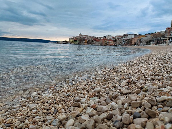 Oblázková pláž se táhne podél průzračně klidného moře