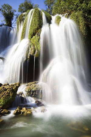 Vysoký vodopád s několika proudy vody stékajícími po skalách obrostlých zelení