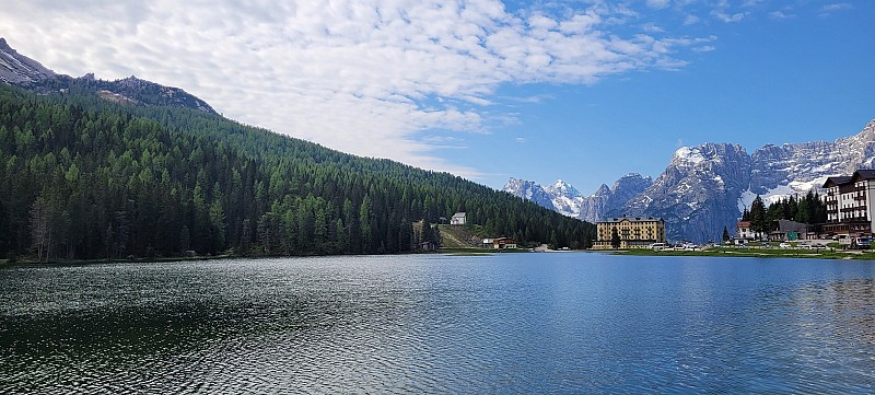 Klidná hladina jezera obklopená zelenými lesy a horskými štíty