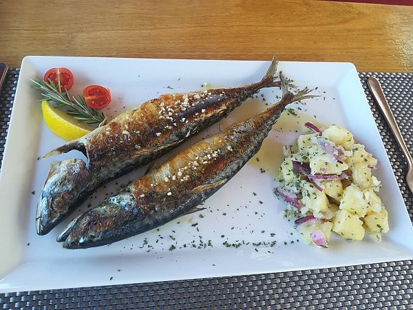 Na talíři jsou dvě grilované makrely s bramborovým salátem, citronem a zeleninovou ozdobou