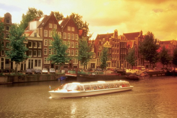 Loď na kanálu lemovaném cihlovými domy při západu slunce