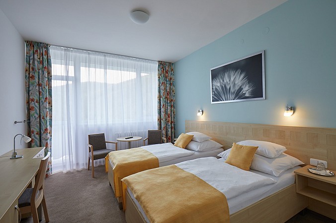 Útulný hotelový pokoj se dvěma oddělenými lůžky, světle modrými stěnami a balkonem