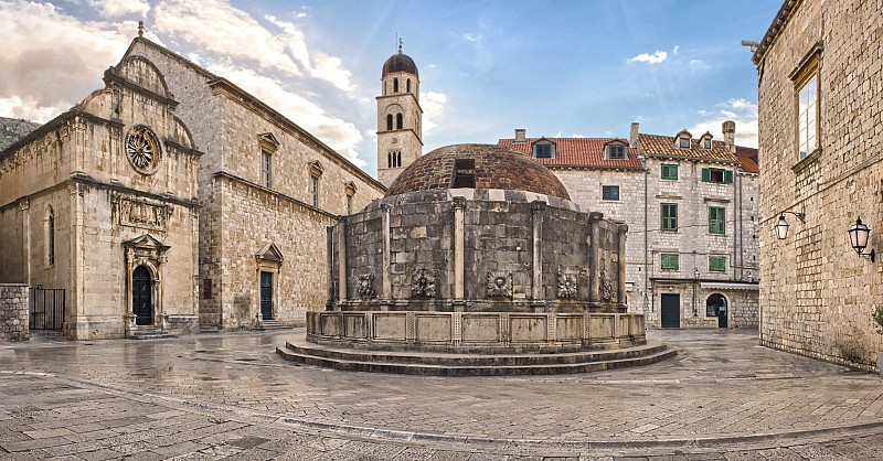 Kamenná kašna uprostřed náměstí obklopeného historickými budovami