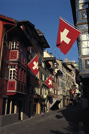 Úzká ulice lemovaná dřevěnými domy se švýcarskými vlajkami visícími z fasád