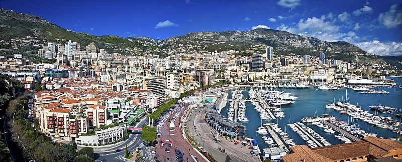 Panoramatický pohled na Monako s přístavem Port Hercule plným jachet a hustou městskou zástavbou v pozadí