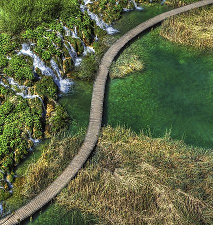 Dřevěná lávka klikatící se mezi zelenou vegetací a průzračně zelenou vodou jezera